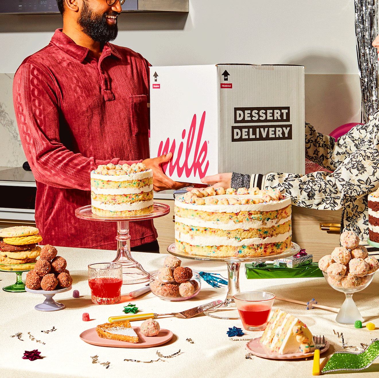 A dessert spread featuring the 10 inch and 6 inch birthday cakes on dessert trays, surrounded by cake truffles, assorted cookies, and milk bar pie.