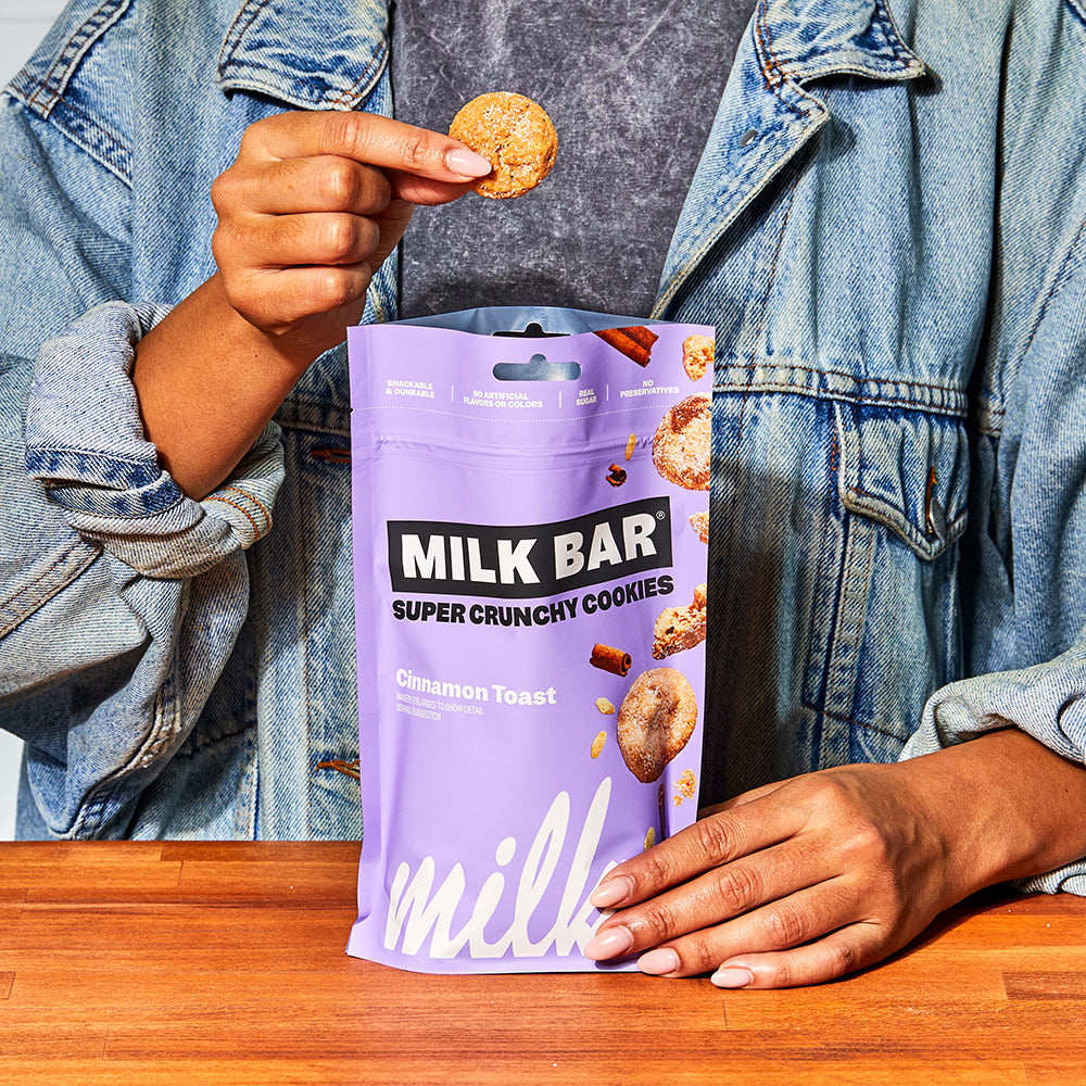 Front view of a bag of cinnamon toast crunchies, with a human holding up a single cookie above the bag