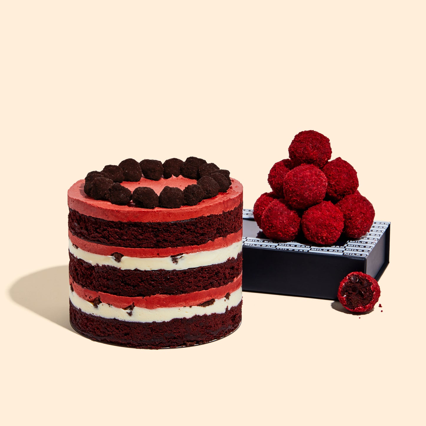 A pile of Red Velvet Cake Truffles sitting on top of their packaging next to the 6" Red Velvet Cheesecake Cake.